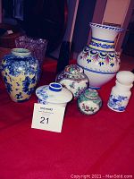 Seven ceramic decorative items including vases and ginger jars on red cloth, showing different colors and patterns