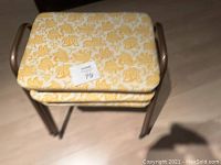 Photo showing the three vintage stacking stools stacked together, highlighting the yellow floral patterned cushioned seats and bronze metal tubular frames.