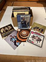 Photo showing a cardboard box filled with 37 LP records with visible album covers of The Lettermen, The Bee Gees, George Benson, and an additional album titled 0ncerise, alongside a 1968 McLeans magazine placed in front of the box.