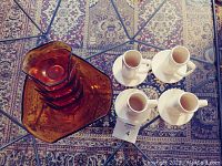 Overhead view of the four amber glass dessert bowls stacked within a larger serving bowl next to four off-white porcelain cups each paired with a saucer.