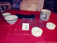 Porcelain bowls with geometric pattern, cylindrical decorated porcelain vase, two glass trays, and two ashtrays on red cloth surface
