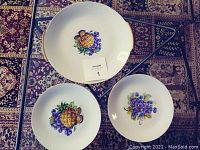 Cake plate and two dessert dishes showing pineapple and grape fruit designs with gold trim on white porcelain.