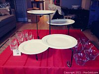Photo showing 6 crystal highball glasses, 6 glass dessert bowls, 4 decorated white on white plates on a four-tier articulating black metal plate stand, displayed on a red tablecloth.