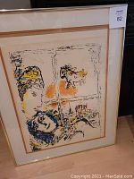 Framed print artwork under glass in gold-tone frame with white mat leaning against wall