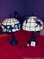 Pair of two faux Tiffany style lamps on red tablecloth, visible ornate dark metal bases, stained glass style shades with floral and leaf designs