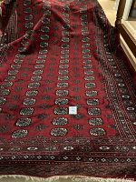 Photo showing overall ruby red Persian-style synthetic rug with medallion and border pattern spread out on floor
