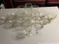 Photo showing the entire collection of 14 vintage Cornflower crystal stemware glasses arranged on a white surface including 7 wine glasses, 1 sherry glass, and 6 champagne cups, all with etched cornflower floral patterns.