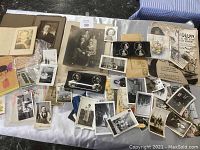 Overview of table covered with assorted antique black and white photographs, photo negatives, postcards, and ephemera