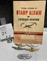 Photo of the Tydol Flying Stamp Album booklet with aviation-themed cover and three airline wing pins in front.