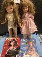 Front view of two Gotz dolls posing, standing side by side, with two vintage doll magazines laid out in front