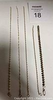 Five silver chains laid out flat on white background, including three longer ones and two shorter ones with different designs.