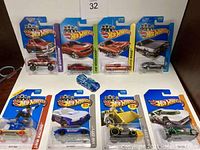 Nine Hot Wheels cars, eight sealed in blister packs and one open stock car visible on white table surface.