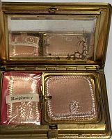 Open compact showing original powder puff pads and raspberry blush pad, beveled mirror inside lid.