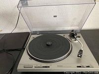 Front view of turntable with dust cover open showing platter, tonearm, controls