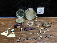 Two glass trinket boxes—one octagonal with etched mirror lid (mirror broken), one round—and assorted jewelry arranged in front including watches, bracelets, earrings, necklaces, rings, and pendants