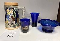 Photo showing front view of vintage textured beer stein from Japan and three deep sapphire blue glass items: small bowl, shot glass, and vase.