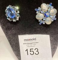 Two vintage brooches displayed on black velvet, emphasizing the blue stones and prong settings.