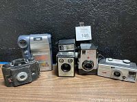 Group shot of six vintage cameras arranged in one row showing brands and physical condition.