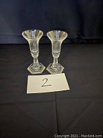 Two clear stem shot glasses with hexagonal bases on black background, numbered '2'.