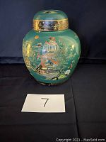 Front view of green Carltonware urn showing the detailed Asian landscape artwork and gold decorative band on lid.