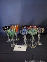 Eight coloured crystal stemmed glasses arranged in two sets against a dark background