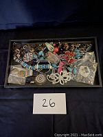 Tray filled with vintage costume jewelry including various bracelets, brooches, earrings, and necklaces in mixed metals, stones, and colors.