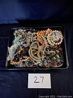 Top view of a tray holding multiple pieces of vintage costume jewelry including bracelets, necklaces, earrings, and brooches.