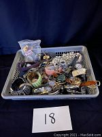 Basket filled with various wristwatches, bracelets, necklaces, and other jewelry items arranged loosely showing diverse styles and colors.