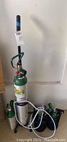 Full view of four oxygen tanks, one large with metal wheeled stand and three smaller with green regulators and base stands