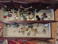 Open drawers of wooden jewelry case showing organized sterling silver button covers and colorful button covers