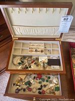 Open top view of wooden jewelry box showing ring rolls, divided compartments, and lower drawer filled with jewelry