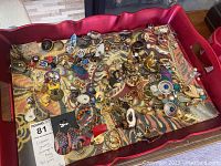 Top view showing a large assortment of over 30 pairs of costume jewelry earrings in multiple colors and styles on a red tray with a tan pattern fabric liner.