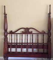 Front view of mahogany four post queen size headboard with turned spindles and decorative carved wood at top.