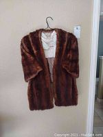 Brown fur shawl hanging on wall on a black hanger, showing the full front.