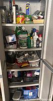 Cabinet shelves filled with various hardware and home repair supplies including canisters, bottles, rolls of tape, plastic containers, and boxes.