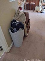 Gray storage basket with dark blue heating pad and beige pillow inside, standing against a wall in a carpeted hallway.