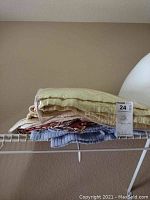 Stack of four folded quilts in beige and cream colors on a wire shelf