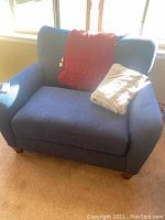 Front angle view of the oversized blue fabric armchair with red and beige throws placed on the seat.