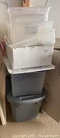 Stack of various plastic totes and storage bins in white, translucent, and gray colors.