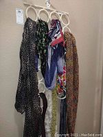 Scarves and belts hanging on a white plastic hanger with multiple ring holders showing various scarf patterns and two belts.