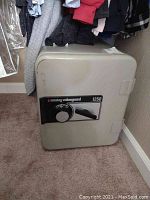 Photo of a light gray Sentry ValueGuard 1250 safe with a combination lock and handle, positioned against a wall near hanging clothes.