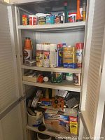 Full view of cabinet shelves showing assorted spray paint cans, mineral spirits, caulk, cleaning and painting supplies.
