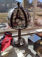 Full view of the lamp on a table showing the stained glass hummingbird design and decorative metal base.