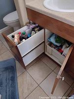 Second bathroom cabinet drawer with additional cleaning products, towels, plastic containers