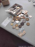 Coins laid out loosely on a surface alongside a small box filled with additional coins and paper currency scraps