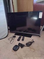 Vizio TV 32 inch flat screen with two remotes, Roku device, and power cords on carpeted floor.