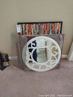 Display of large framed puzzle, white circular mirror, mesh panel, and fabric panel grouped on floor against wall