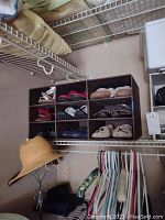 Closet shelf with shoe organizer containing mostly neutral and dark colored women's shoes and a beige sun hat hanging below