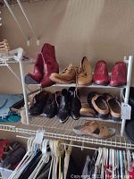 Full view of eight pairs of women's shoes on metal shelving, various styles and colors including red boots, tan boots, red slip-ons, black shoes, and sandals.