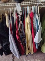 Photo of women's tops and sweaters hanging on hangers on a clothes rack showing variety of colors and styles.